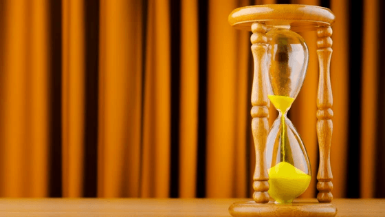 Sand flowing through an hourglass in front of a curtain