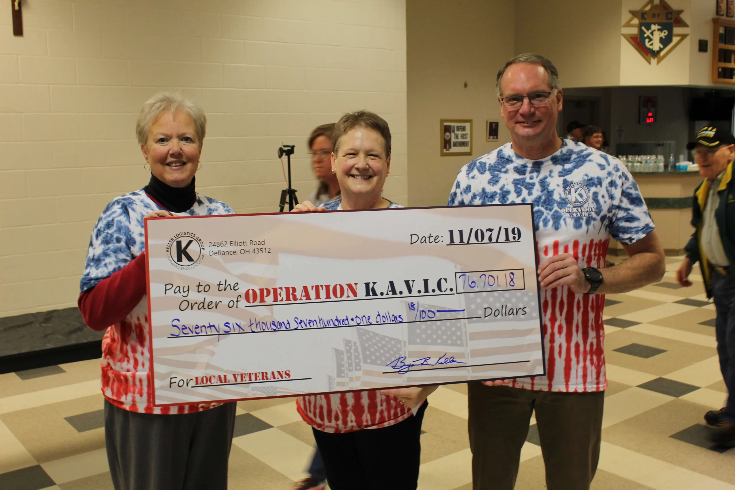 Three people in Operation K.A.V.I.C. shirts hold a large check for money being donated to local veterans from Keller Logistics Group