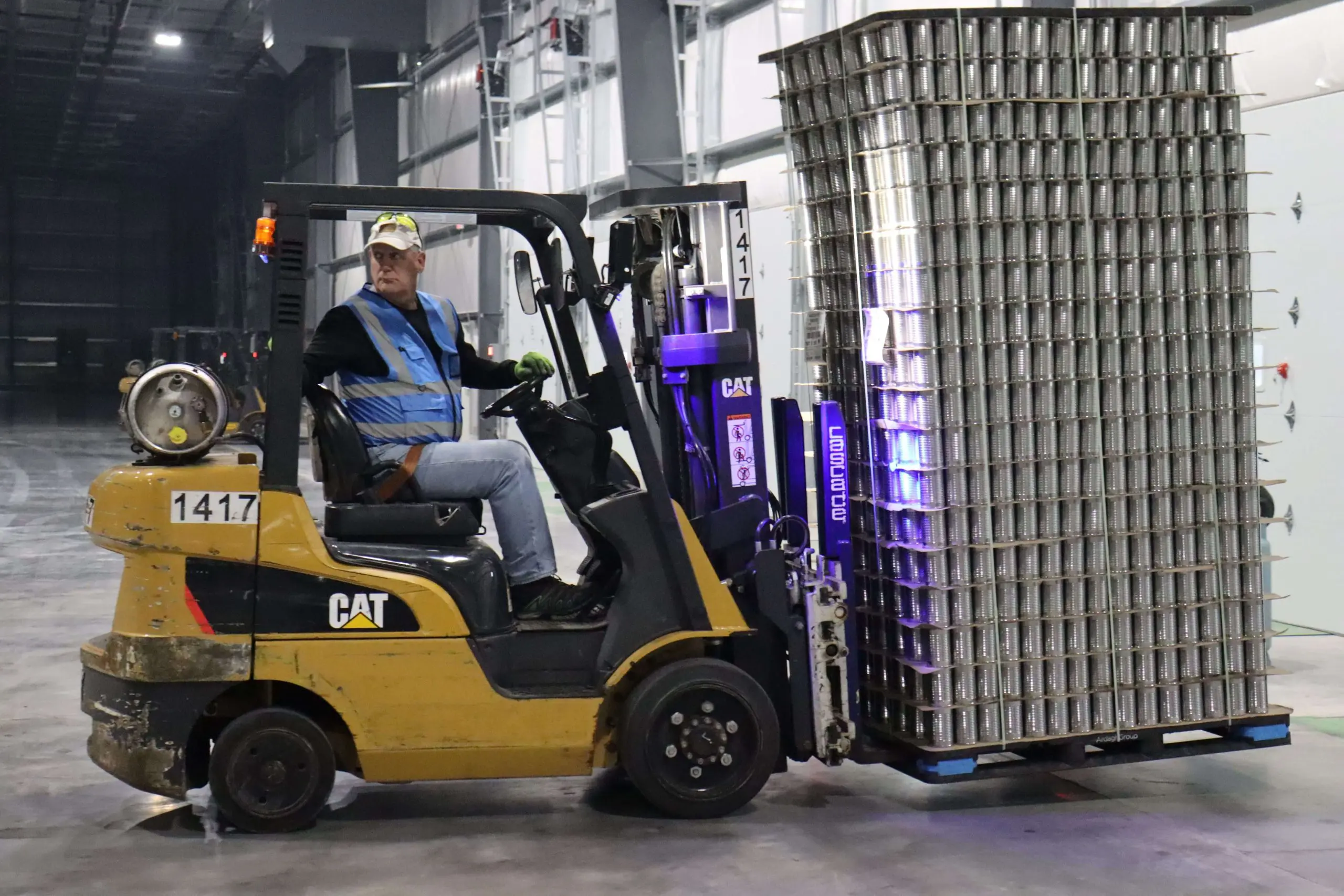 A man on a forklift moving a pallet of cans inside a warehouse